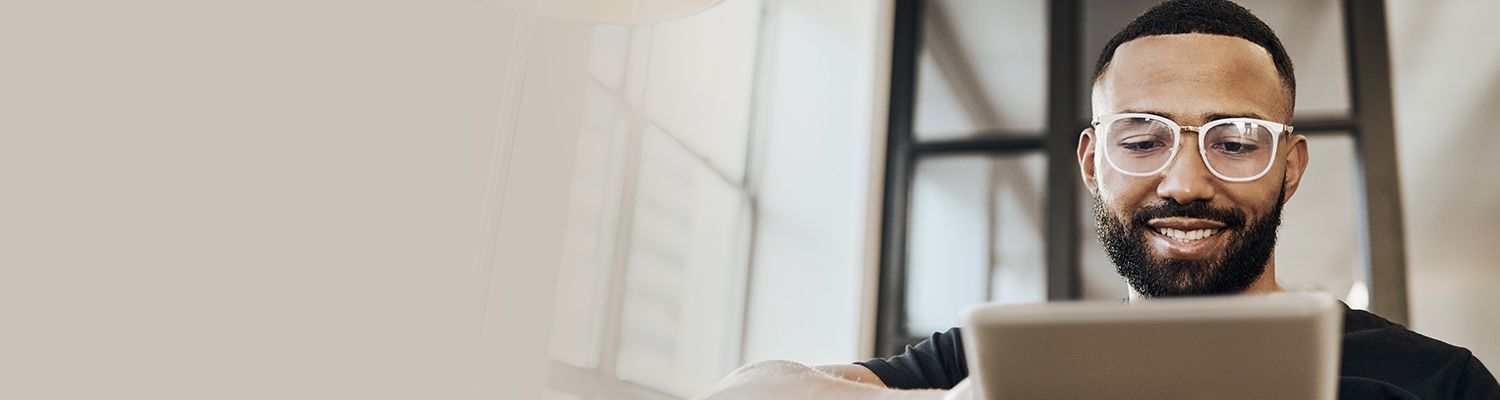 A bearded man wearing glasses is seated while looking at a device screen.